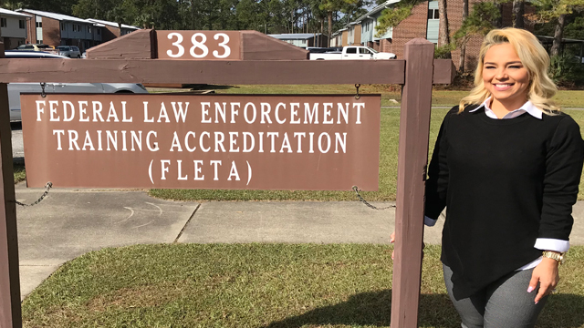 Crystal Johnson stands next to the Federal Law Enforcementing Training Accrecitation FLETA sign