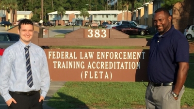 Ben Reynolds and James Mays stand by the sign to the Federal Law Enforcement Training Accreditation (FLETA) Ben Reynolds and James Mays stand by the sign to the Federal Law Enforcement Training Accreditation (FLETA)