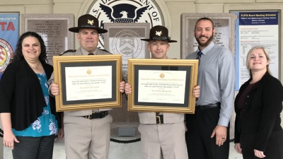 Representatives from the United States Customs and Border Protection hold the two FLETA Accreditation Certificates