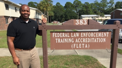 Sean Jones, FLETA Staff Assistant, stands next to the Federal Law Enforcement Training Accreditation (FLETA) sign