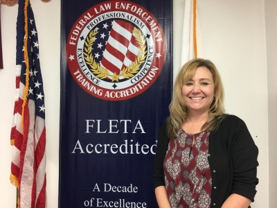 Jennifer Kasper standing next to the FLETA Accredited banner in the Office of Accreditation 